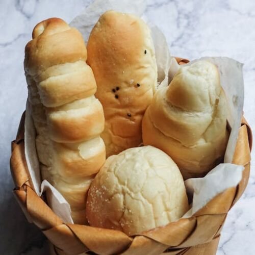 A variety of freshly baked breads in a wooden basket, displayed on a marble surface.